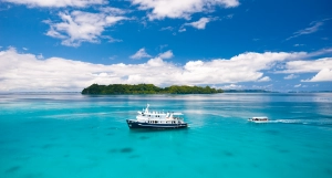 Aerial image of Ocean Hunter Palau, Palau's premier liveaboard in turquoise waters in front of Ulong Island, the dive boat approaching from the right