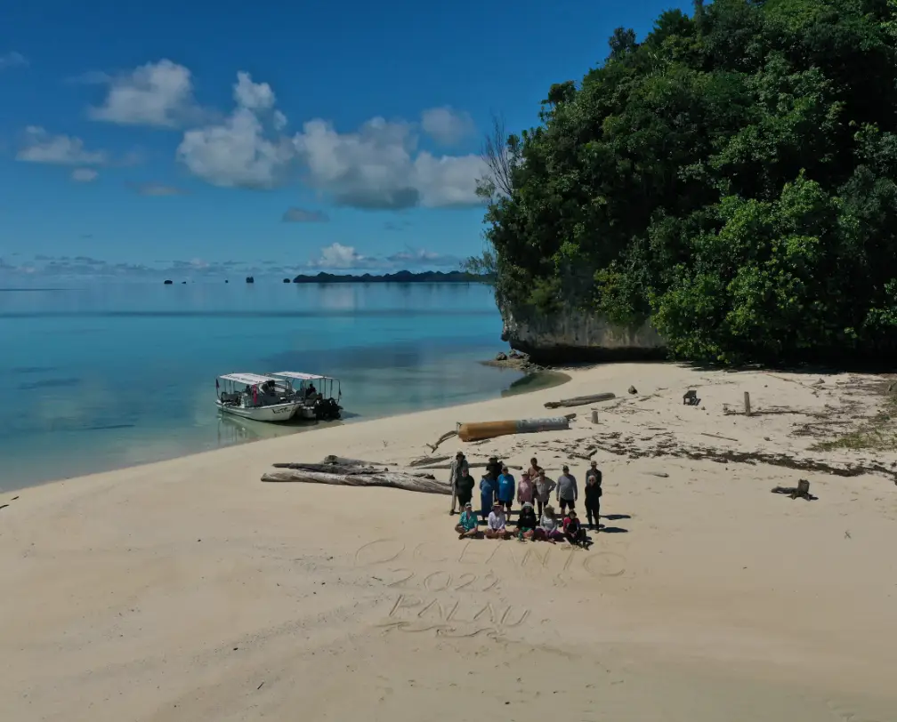 group od Fish 'n Fins divers in Palau on a sandy beach with boat and Rock Islands and blue skies in the background