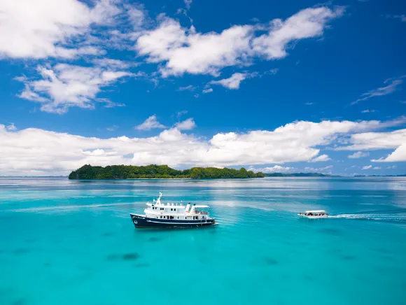 photo of Palau's primer liveaboard, the Ocean Hunter in turquoise waters in front of and island fully visible in the background and its Chase boat approaching 