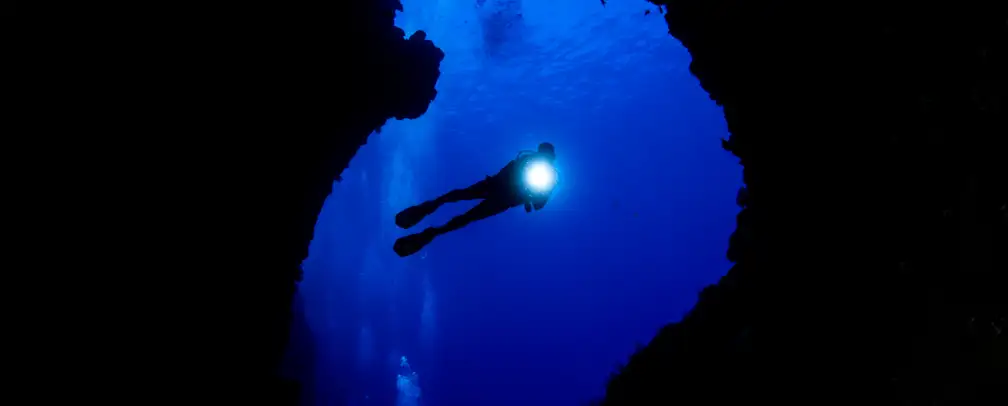 diver with torch shining light towards the camera in the large entrance of an underwater cave