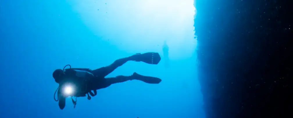 scuba diver perfectly buoyant in from of a steep wall in Palau shining his dive light at the camera