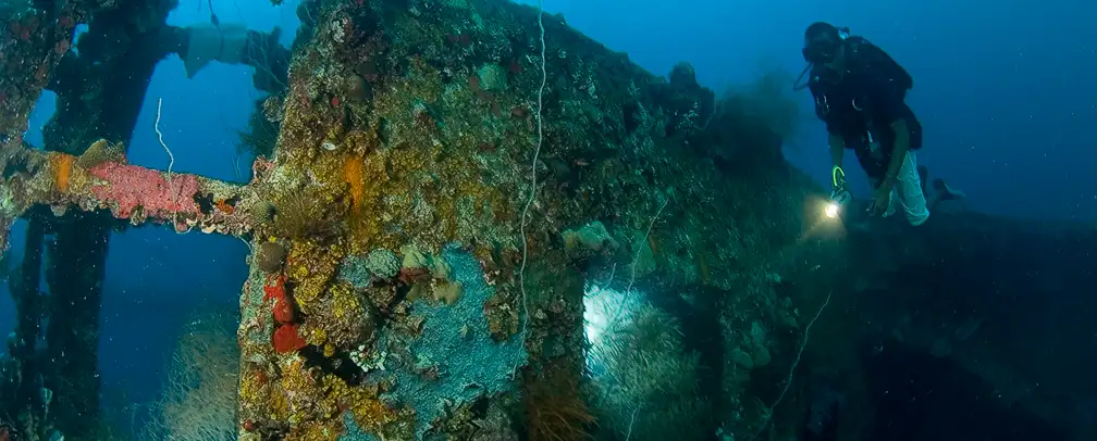 world war 2 wreck in Palau underwater on its side and a diver with a torch exploring it