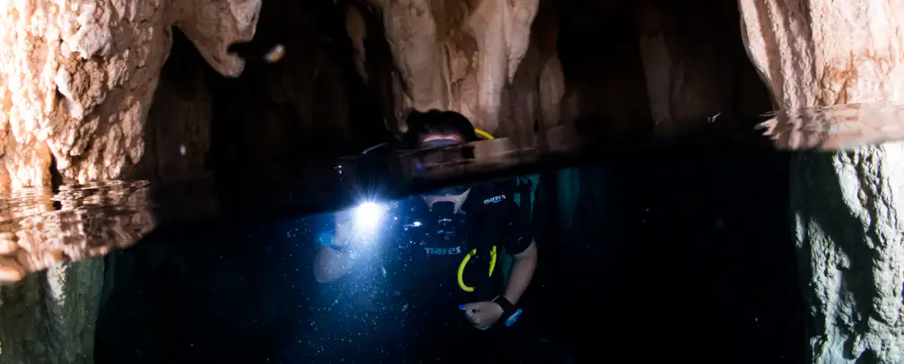 Split photo, half on top, half underwater of a diver in Palau's famous Chandelier Cave