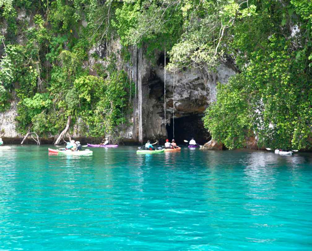 A group of kayaks with paddlers ebetring a cave in the Rock islands