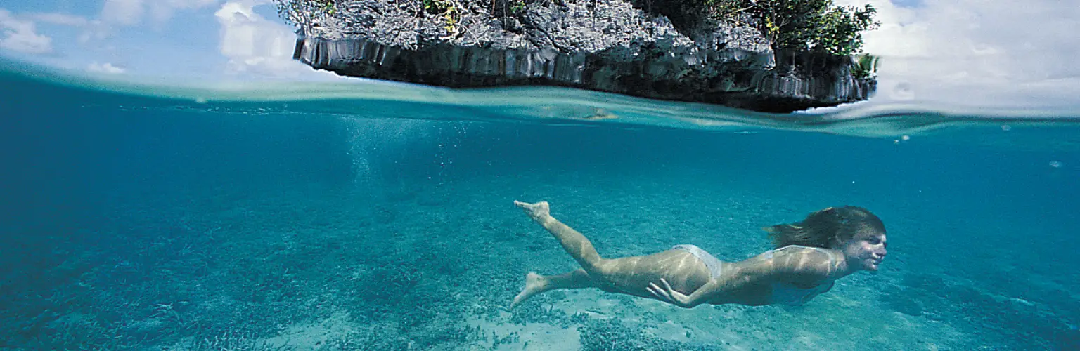 underwater photo of a female snorkeler free diving in shallow water in front of a Rock island in Palau
