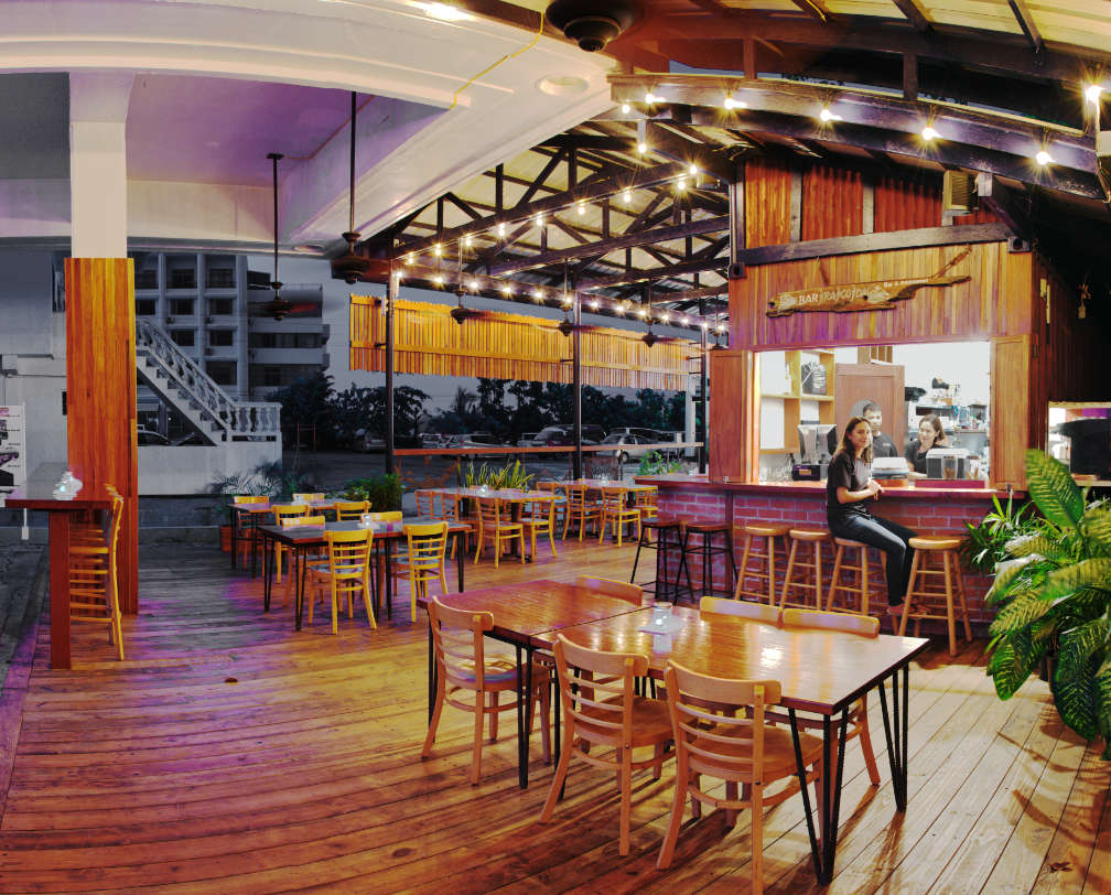 Inside Barracuda Restaurant, showing tables and chairs, looking towards the the bar and the beer dispenser, staff sitting in front of the bar