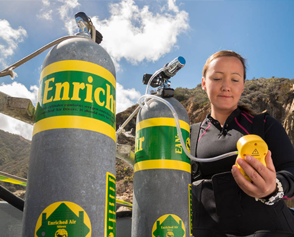 Woman with 2 nitrox tanks checking the oxygen content