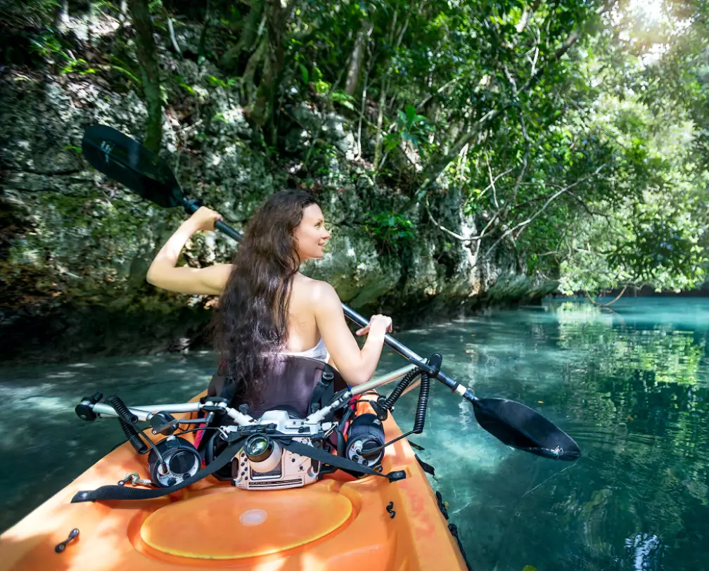 a woman in an orange kayak gliding through the tropical forest in Nikko Bay, Palau